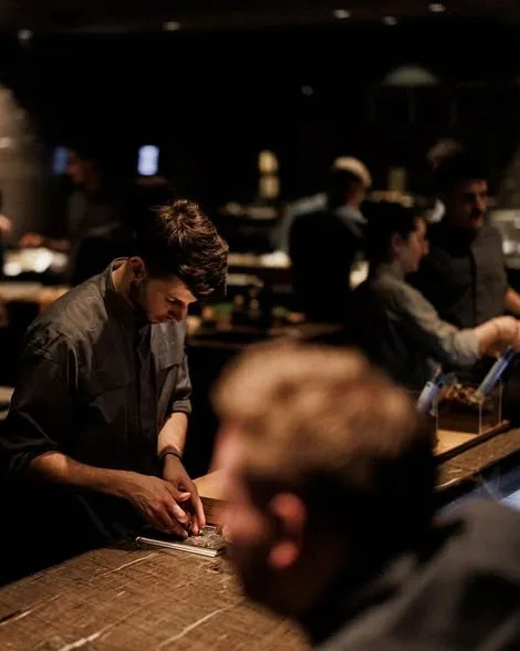A chef finishing a course with tweezers under warm light